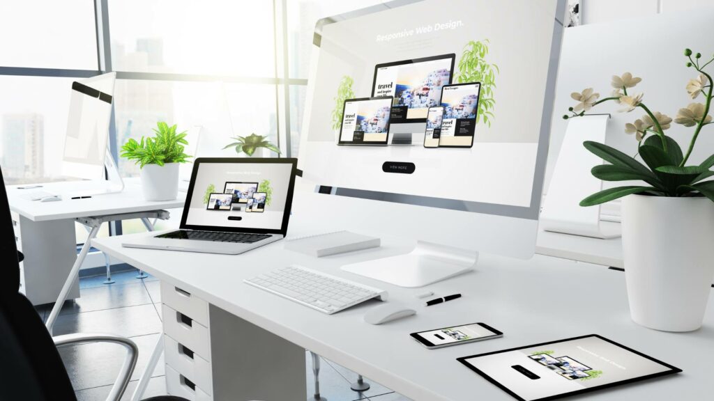 A desktop computer, laptop, tablet, and phone are displayed on a white desk, demonstrating ui/ux design.