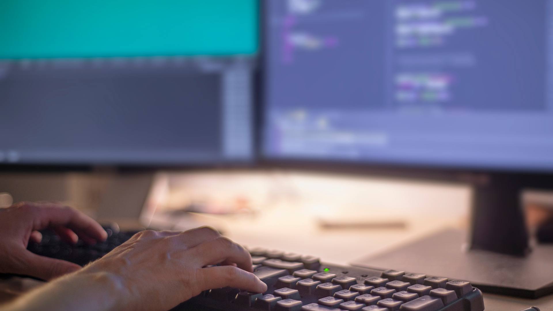 A front end developer works on front end development on a desktop computer with two monitor screens.