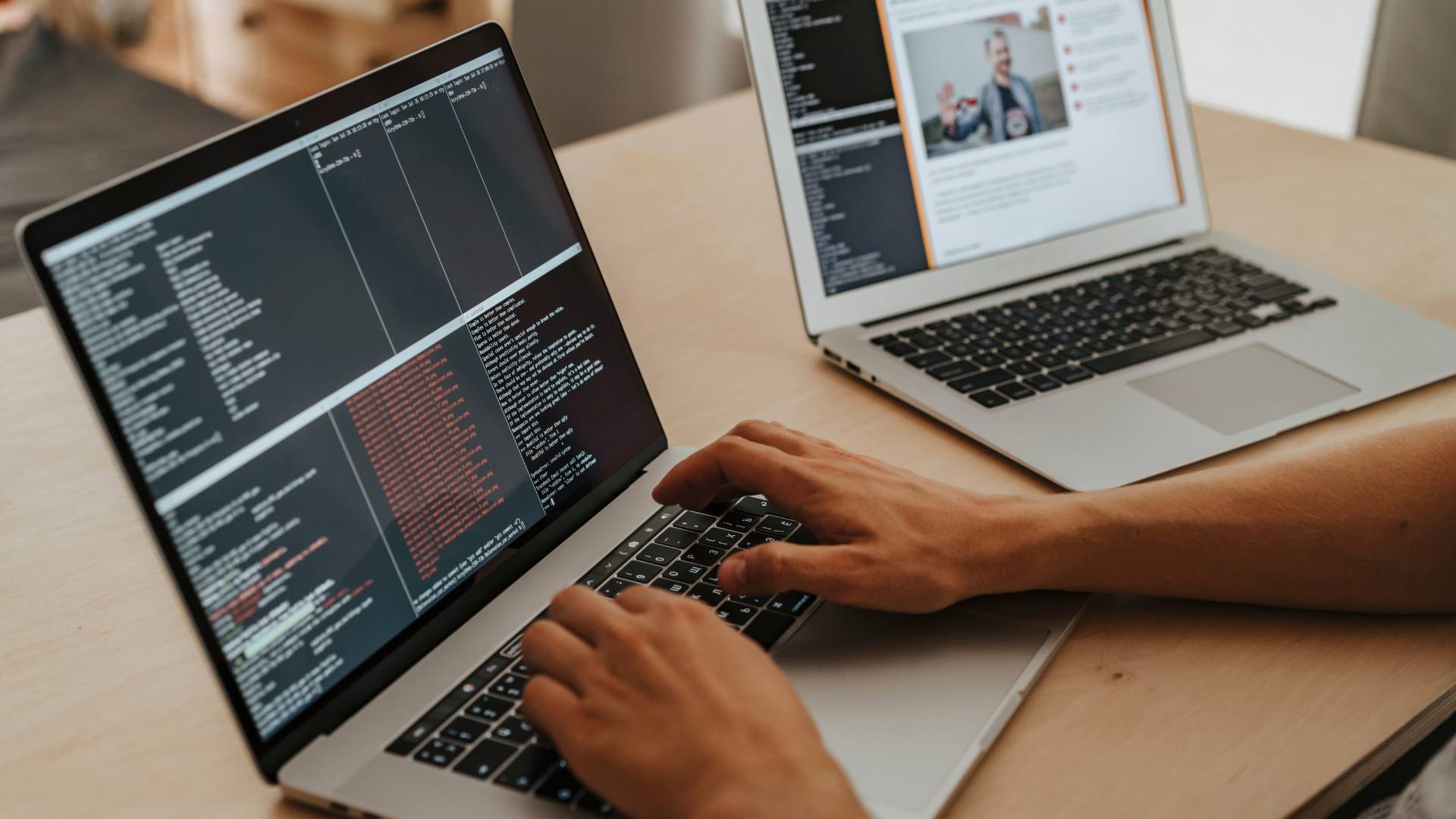 A person works on coding on a laptop, with another laptop open next to them, demonstrating custom web development skills.