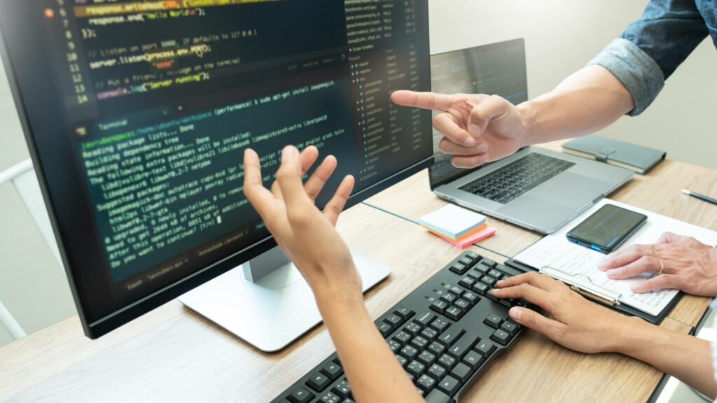 A person works on a desktop on software development code at a wooden table.