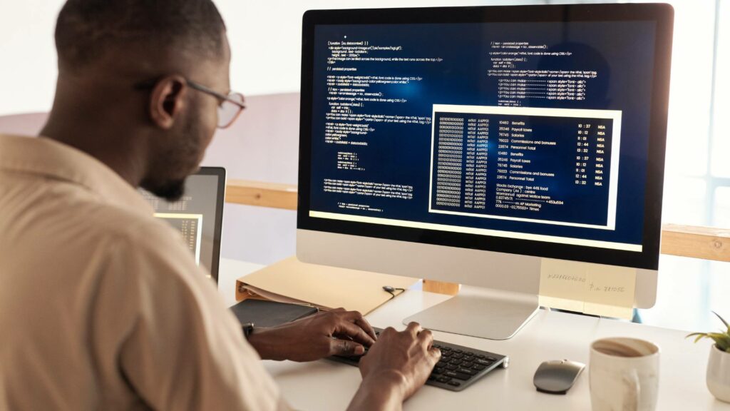 A person works on a desktop computer on software code at a white desk.