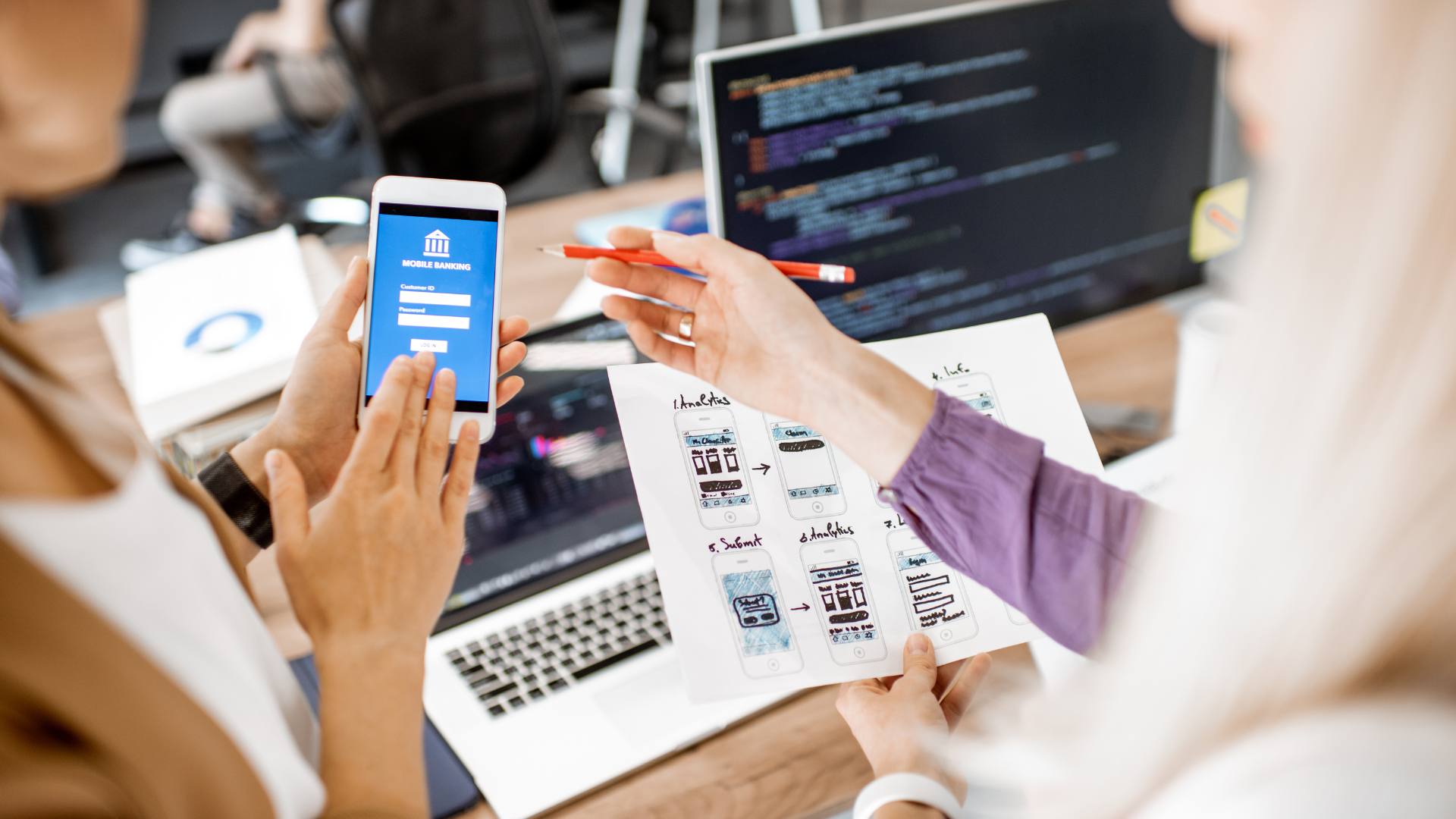 Two people work on web app development on a cell phone and computer desktop.