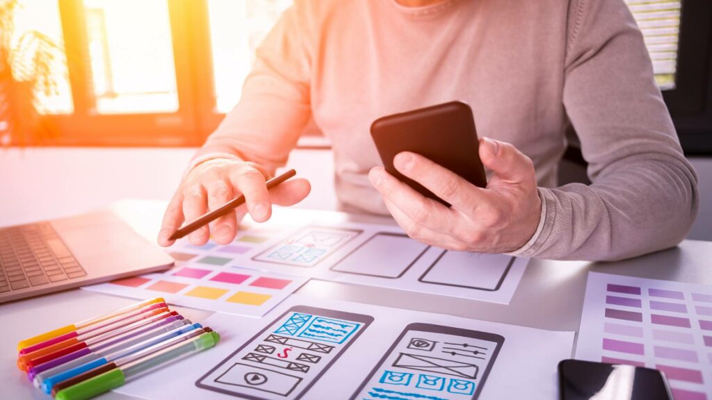 A person holds a phone while looking at a spread of designs, demonstrating mobile app design.